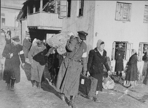 A Jewish policeman helps a family carry their luggage from the Abba Haskel synagogue to the assembly point for deportation in the Kovno ghetto